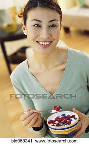 Stock Image - Asian woman eating yogurt with berries. Fotosearch