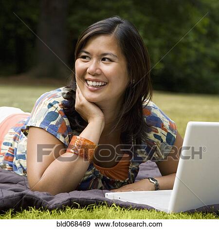 Stock Photo - Asian woman laying in park with laptop. Fotosearch