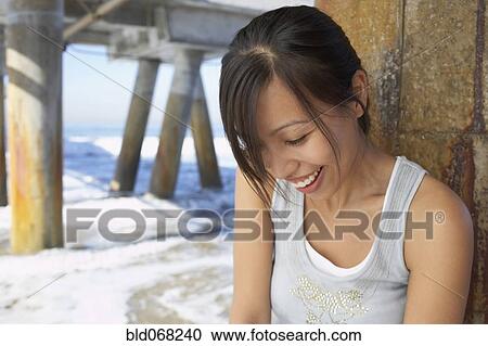 Stock Image - Asian woman smiling near pier at beach. Fotosearch