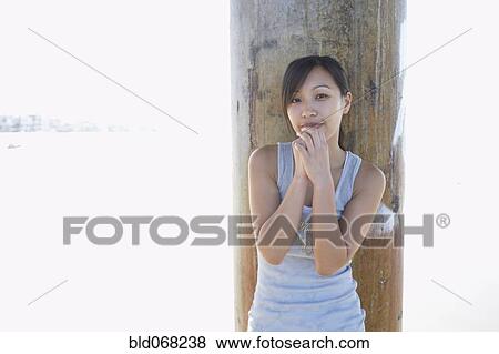 Stock Photo - Asian woman standing in front of pillar at beach. Fotosearch