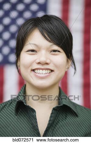 Stock Image - Asian woman standing near American flag. Fotosearch
