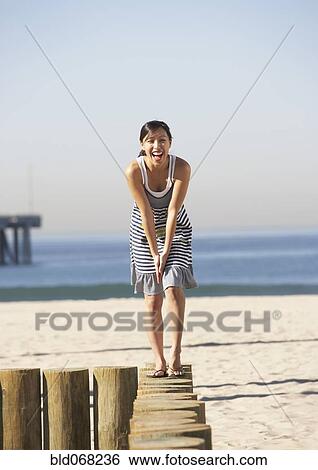 Stock Photograph - Asian woman standing on posts at beach. Fotosearch