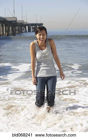 Stock Image - Asian woman wading near pier at beach. Fotosearch
