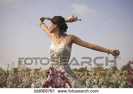 Stock Image - Asian woman with arms outstretched in meadow. Fotosearch
