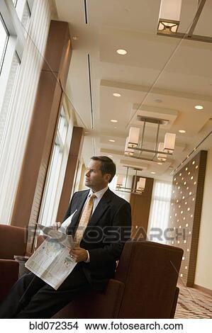 Picture - Businessman holding newspaper in lobby. Fotosearch
