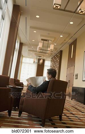 Stock Image - Businessman reading newspaper in lobby. Fotosearch