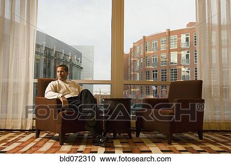 Stock Image - Businessman sitting in hotel waiting area. Fotosearch
