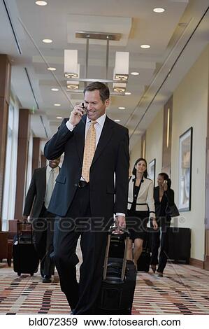 Stock Photo - Businessman talking on cell phone and pulling suitcase down corridor. Fotosearch