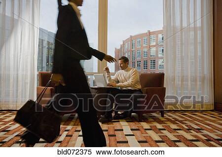 Stock Photography - Businessman working on laptop in waiting area near window. Fotosearch