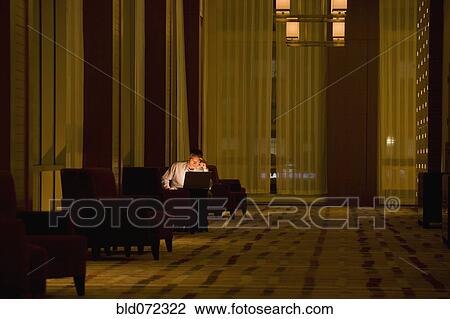Businessman working on laptop late in lobby View Large Photo Image Stock Image - Businessman working on laptop late in lobby. Fotosearch