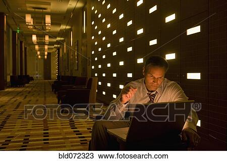 Businessman working on laptop late in lobby View Large Photo Image Stock Image - Businessman working on laptop late in lobby. Fotosearch