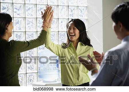 Businesswomen high-fiving next to water cooler View Large Photo Image Stock Photo - Businesswomen high-fiving next to water cooler. Fotosearch