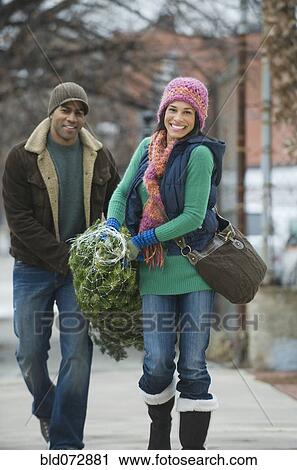 Stock Image - Couple carrying Christmas tree. Fotosearch