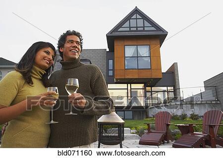 Stock Image - Couple holding wine in front of house. Fotosearch