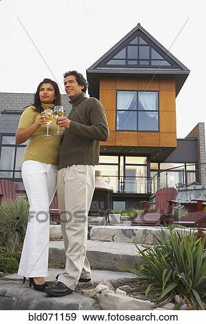 Stock Photo - Couple holding wine in front of house. Fotosearch