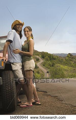 Picture - Couple hugging next to jeep on rural road. Fotosearch