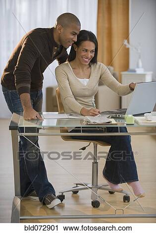 Stock Image - Couple using laptop in home office. Fotosearch