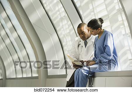 Picture - Doctor and nurse reviewing medical chart in corridor. Fotosearch