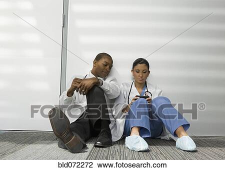 Doctors sitting on floor looking at cell phone View Large Photo Image Stock Image - Doctors sitting on floor looking at cell phone. Fotosearch