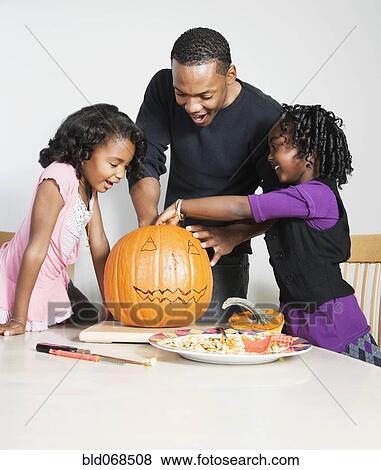 Stock Photo - Father and daughters carving pumpkin. Fotosearch