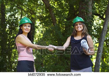 Hispanic architects in green hard hats shaking hands outdoors View Large Photo Image Stock Photography - Hispanic architects in green hard hats shaking hands outdoors. Fotosearch