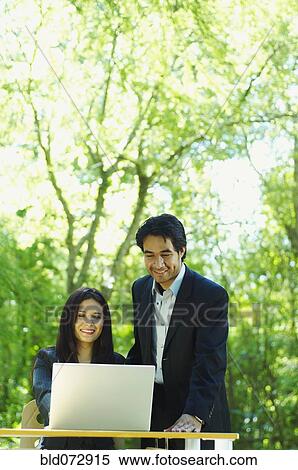 Stock Photography - Hispanic business people using laptop outdoors. Fotosearch