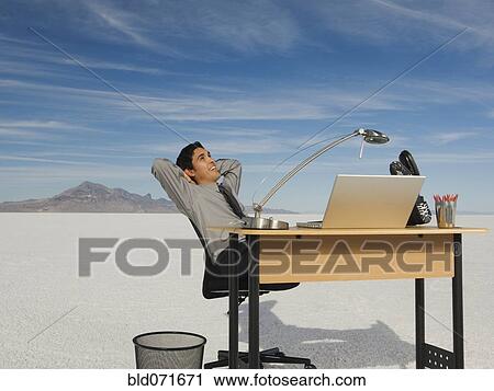 Stock Image - Hispanic businessman at desk on salt flats. Fotosearch