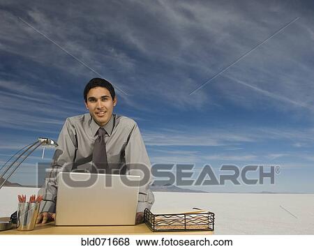 Stock Photo - Hispanic businessman at desk on salt flats. Fotosearch