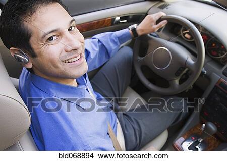 Picture - Hispanic businessman driving with earpiece. Fotosearch