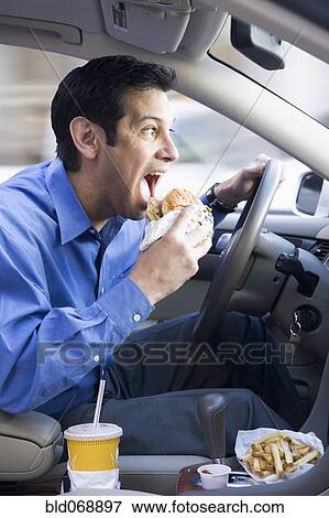 Stock Photo - Hispanic businessman eating and driving. Fotosearch