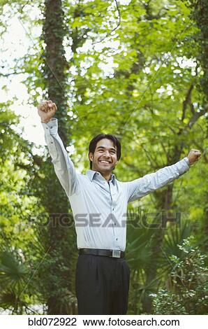 Stock Image - Hispanic businessman in woods with arms outstretched. Fotosearch