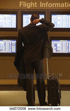 Stock Photo - Hispanic businessman looking at flight information monitors. Fotosearch