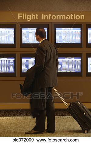 Stock Photo - Hispanic businessman looking at flight information monitors. Fotosearch