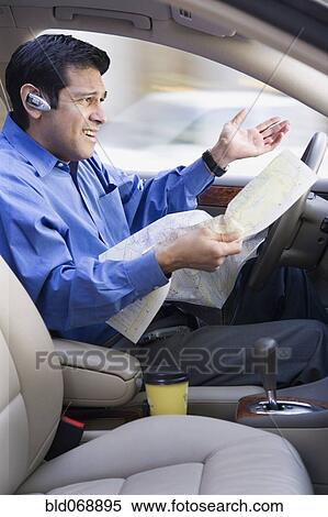 Stock Photography - Hispanic businessman looking at map and driving. Fotosearch