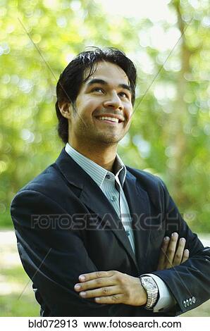Stock Image - Hispanic businessman looking up with arms crossed. Fotosearch