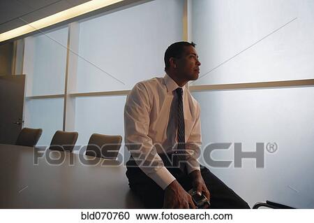 Stock Image - Hispanic businessman sitting on conference table. Fotosearch