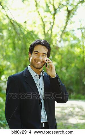 Picture - Hispanic businessman talking on cell phone outdoors. Fotosearch