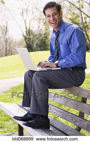 Stock Photo - Hispanic businessman using laptop outdoors. Fotosearch