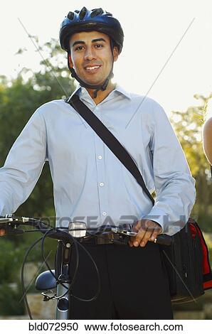 Stock Image - Hispanic businessman wearing bike helmet and holding bike. Fotosearch