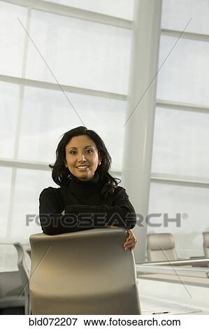 Stock Photo - Hispanic businesswoman leaning on conference room chair. Fotosearch
