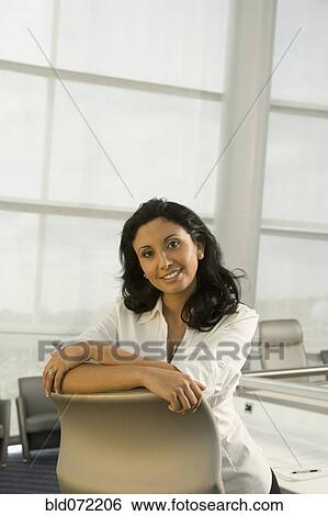 Stock Photograph - Hispanic businesswoman leaning on conference room chair. Fotosearch
