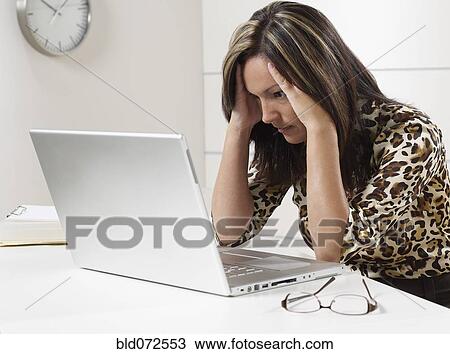 Stock Image - Hispanic businesswoman looking at laptop with head in hands. Fotosearch