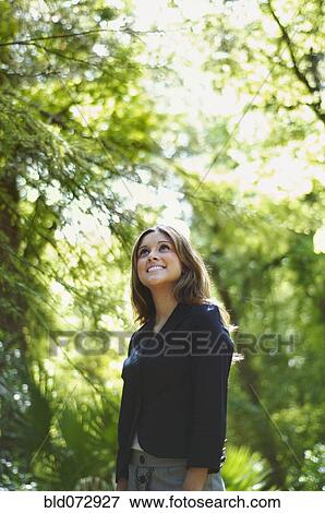 Stock Photo - Hispanic businesswoman looking up in woods. Fotosearch