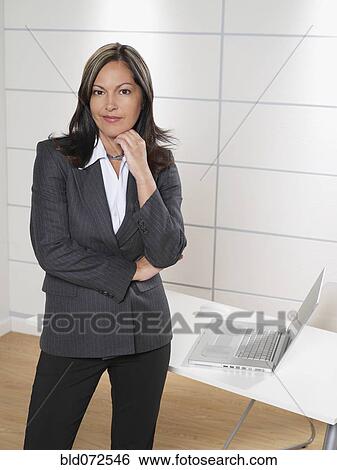 Stock Photograph - Hispanic businesswoman posing by office desk. Fotosearch