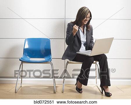 Stock Image - Hispanic businesswoman using laptop in waiting room. Fotosearch