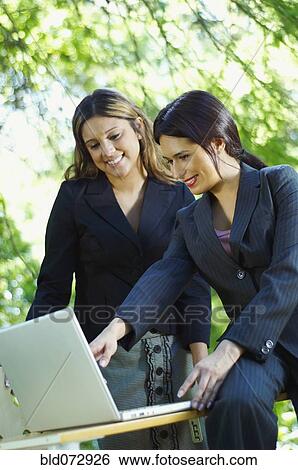 Stock Photograph - Hispanic businesswomen using laptop outdoors. Fotosearch