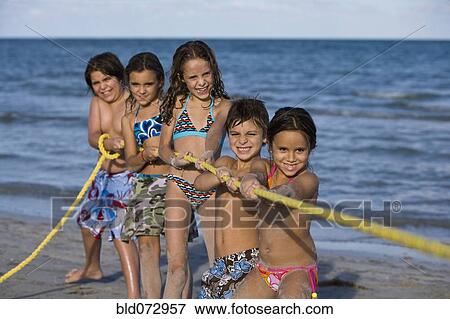 Stock Photo - Hispanic children playing tug-of-war on beach. Fotosearch