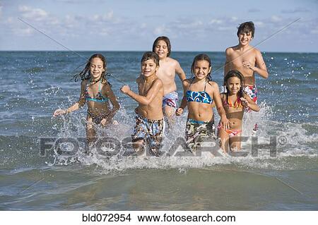 Picture - Hispanic children running through ocean surf. Fotosearch