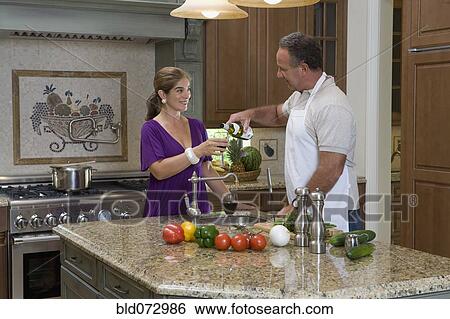 Stock Photograph - Hispanic couple drinking wine and preparing meal in kitchen. Fotosearch