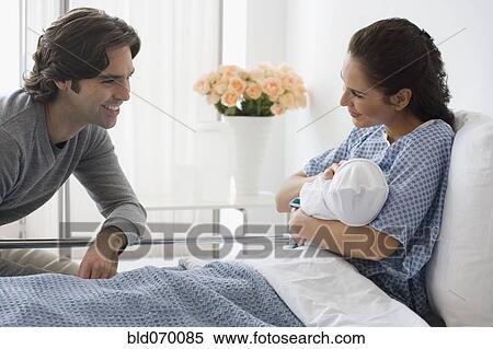 Stock Photography - Hispanic couple holding newborn baby in hospital bed. Fotosearch